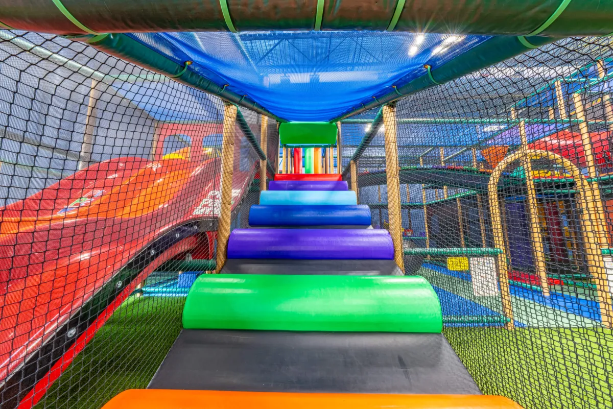 Colorful obstacles along a netted indoor climbing route.
